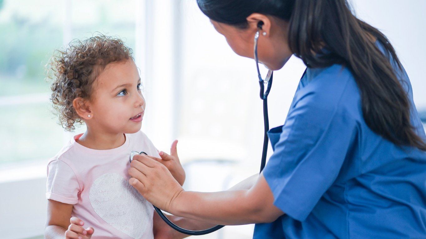 girl toddler with paediatrician in blue scrubs using stethoscope